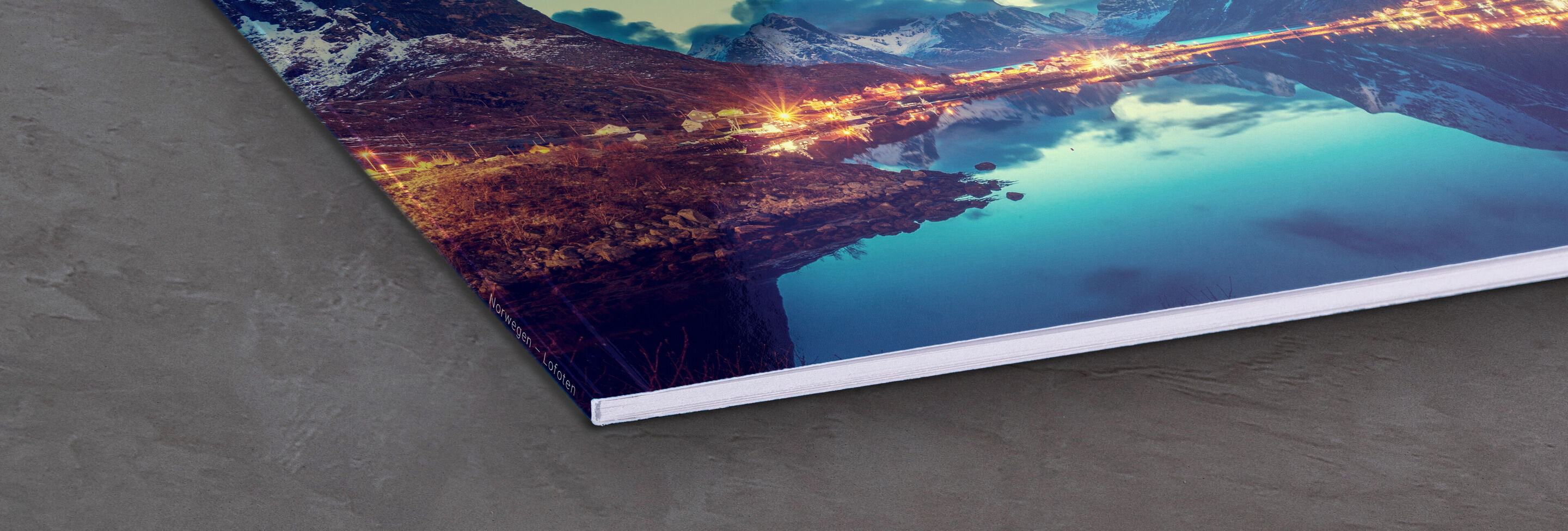 Eine Ecke eines CEWE Fotobuchs mit einem wunderschönen Bild von Bergen und Wasser, das glänzend im Licht reflektiert wird