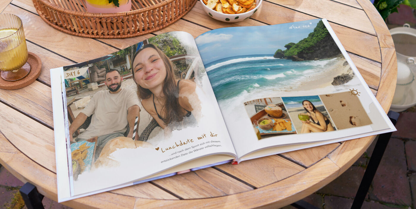 Auf einem Holztisch liegt ein geöffnetes Fotobuch mit Urlaubsaufnahmen.