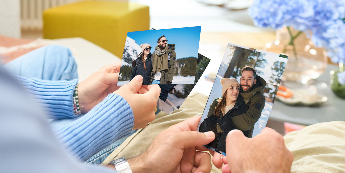 Zwei Personen sitzen nebeneinander und halten mehrere entwickelte Urlaubsfotos aus dem Winter in den Händen