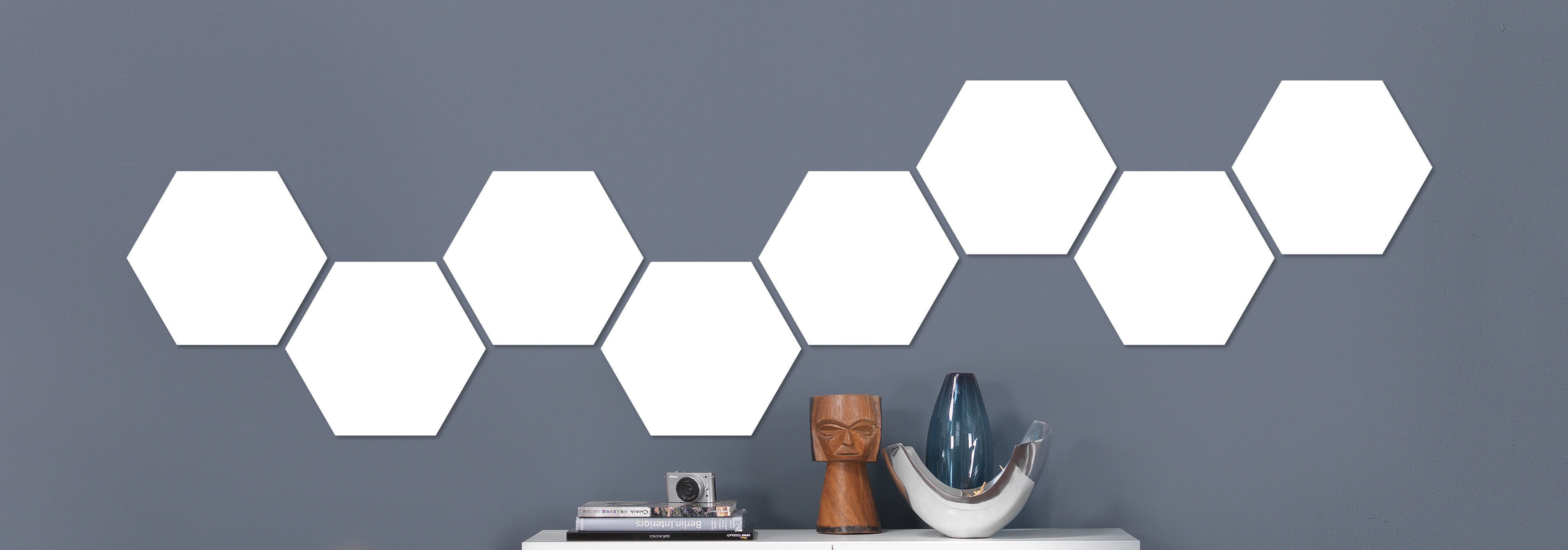 Sechs leere, hexagonale Wandbilder auf grauer Wand angeordnet, darunter liegen Dekorationsgegenstände auf einem Tisch.