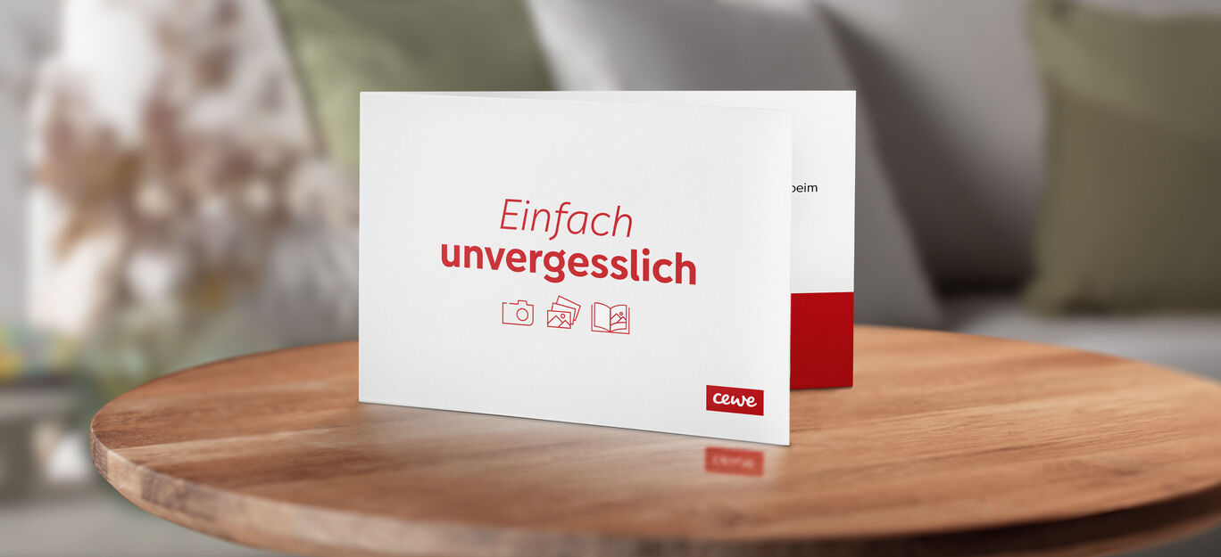 Eine CEWE Grußkarte, die auf einem Tisch liegt, mit den Worten "Einfach unvergesslich" in roten Buchstaben.