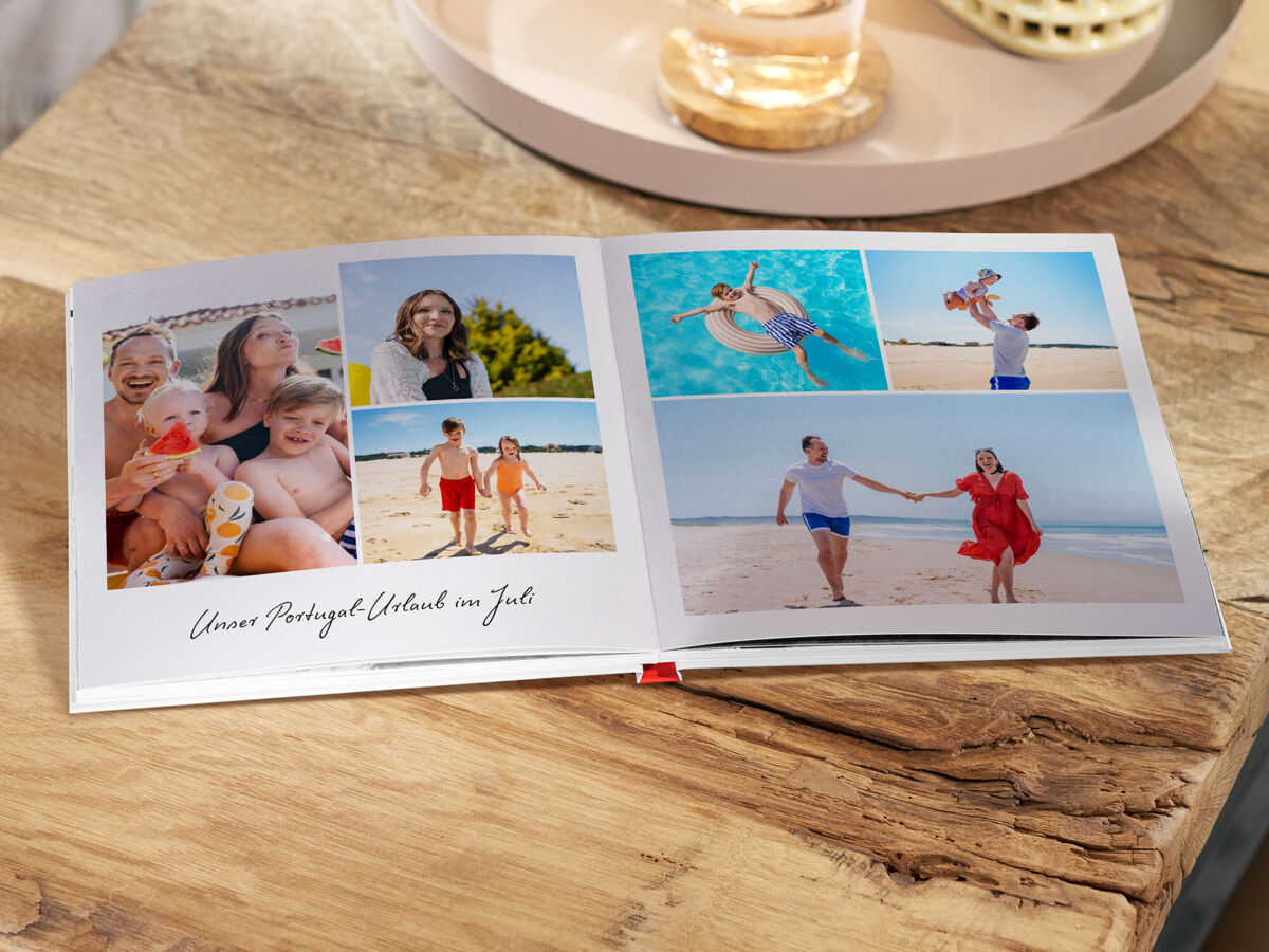 Aufgeschlagenes Fotobuch auf einem Holztisch mit sommerlichen Familien- und Urlaubsfotos am Strand und im Wasser.