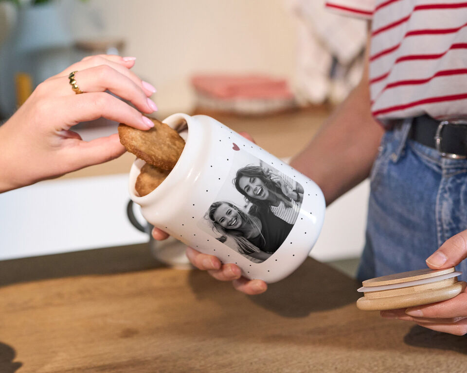 Eine CEWE Keksdose mit persönlichem Foto wird geöffnet und eine Hand nimmt einen Keks heraus