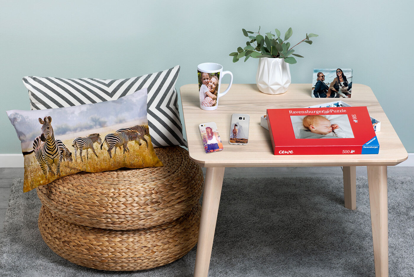 Ein gemütlicher Tisch mit einem Zebra-Kissen, einer Tasse mit einem Foto, einem kleinen Pflanzenarrangement und einem CEWE Fotobuch.