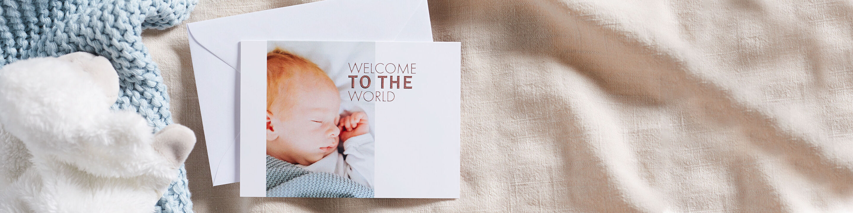 Eine süße Babykarte mit dem Text 'Willkommen in der Welt' auf einem hellen Hintergrund mit einem beruhigenden, weichen Stoff.