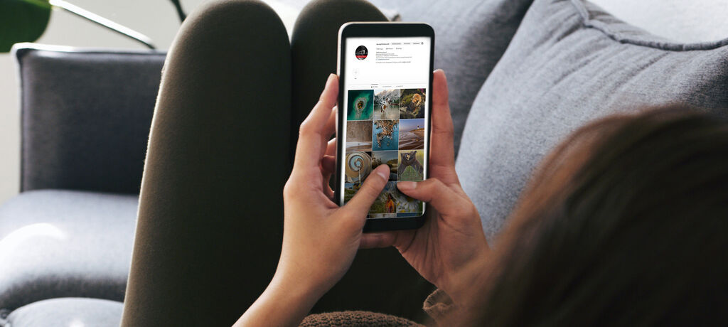 Eine Person sieht sich auf ihrem Smartphone Bilder von Urlaubsmomenten an, während sie entspannt auf einem Sofa sitzt