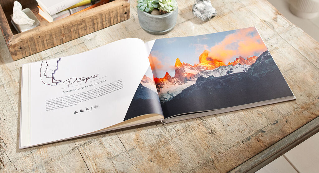 Ein geöffneter CEWE FOTOBUCH auf einem Tisch, der die atemberaubende Landschaft von Patagonien in bunten Farben zeigt. Ein Sonnenuntergang beleuchtet die Berge.