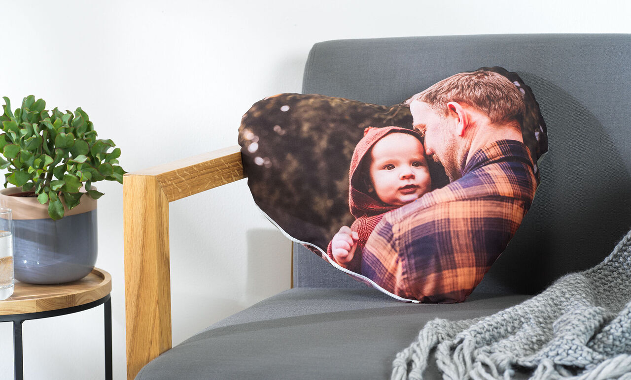 Ein herzförmiges Kissen mit einem liebevollen Foto von einem Mann und einem Kind im Freien.