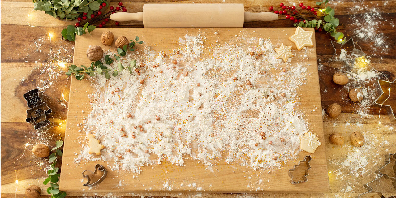 Ein Holztisch mit Mehl, Nüssen und Plätzchenformen für das Backen von Weihnachtsplätzchen