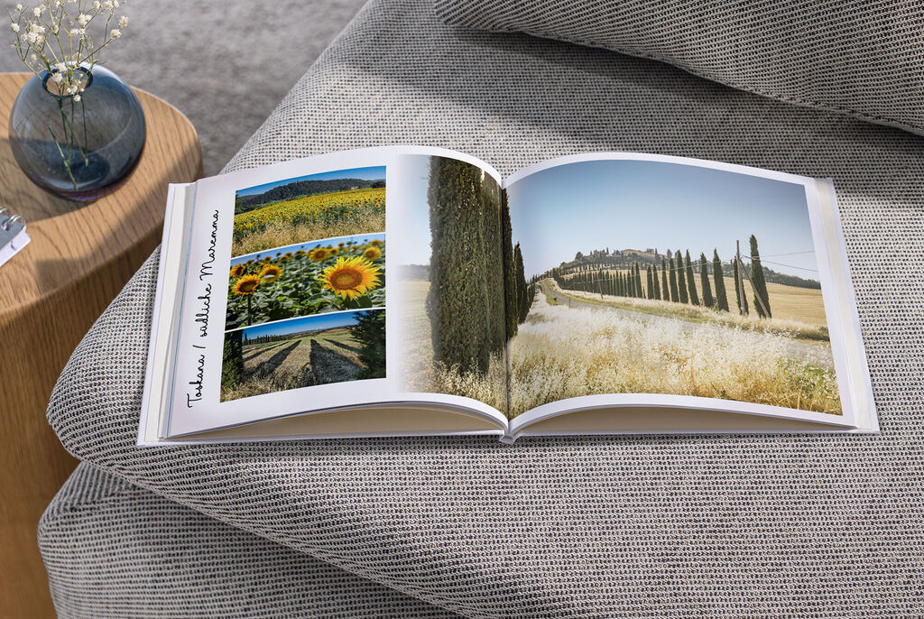 Ein geöffnetes Fotobuch zeigt sonnige Landschaften mit Sonnenblumen und Zypressen. Die Bilder sind farbenfroh und einladend.