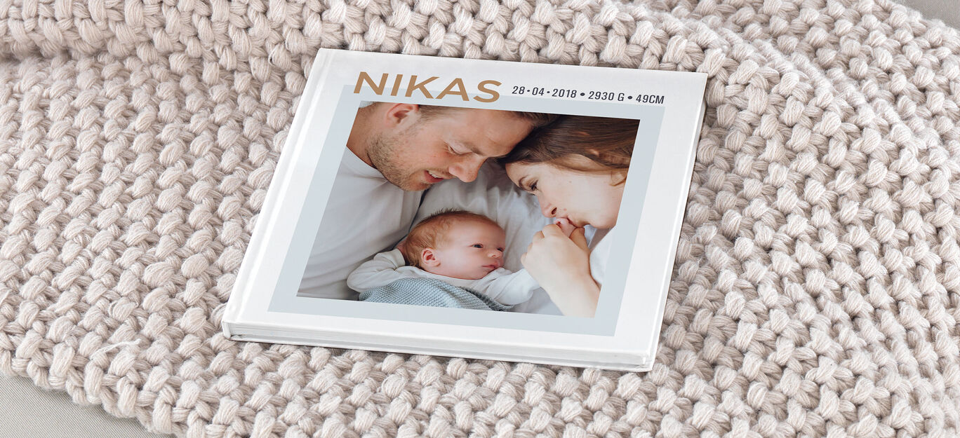 Eltern betrachten liebevoll ihr Baby auf einem Fotobuch.