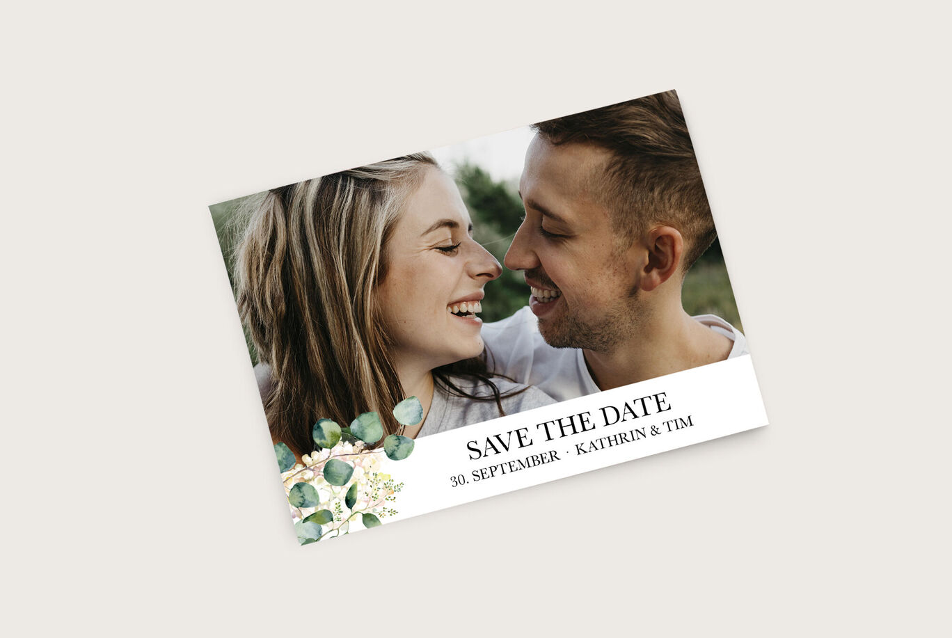 Ein Paar hält sich in der Natur umarmt, um den "Save the Date"-Anlass zu feiern. Elegantes Design mit grünen Elementen und einem wunderschönen Schriftzug.