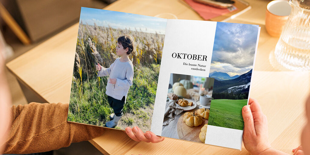 Zwei Personen blättern durch einen Fotokalender, eines der Blätter zeigt eine Landschaft und einen Monat.