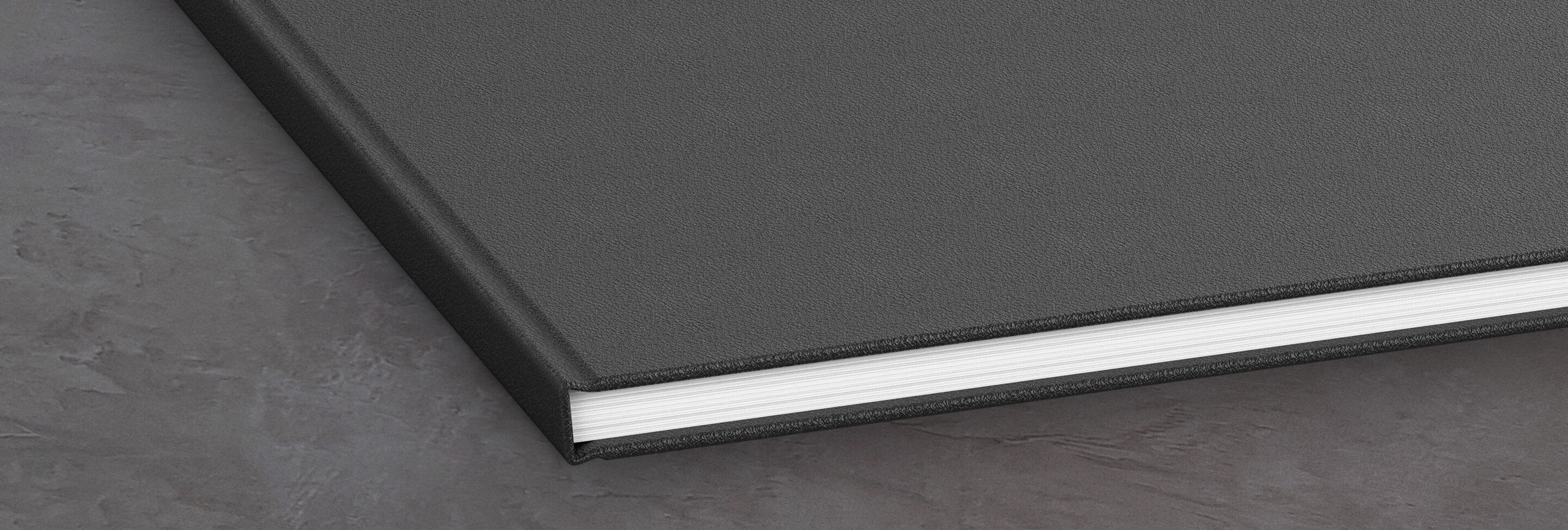 Ein geschlossenes, schwarzes Fotobuch liegt auf einer grauen Oberfläche