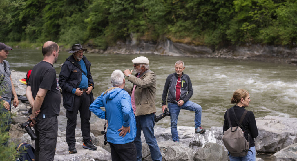 Mehrere Personen in Outdoorkleidung stehen an einem Flussufer und diskutieren.
