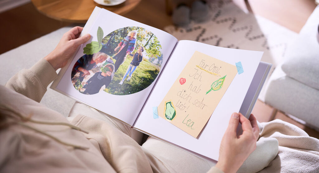Eine Frau hält in ihren Händen ein aufgeschlagenes CEWE FOTOBUCH, das zwei Fotos und einen eingeklebten Brief zeigt.
