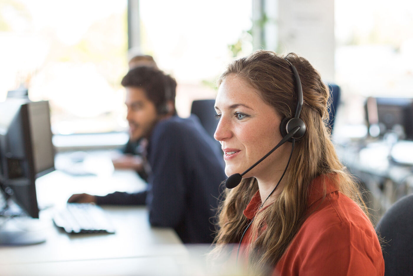 Zwei Mitarbeiter in einem Kundenservice-Büro, die Telefone benutzen und am Computer arbeiten