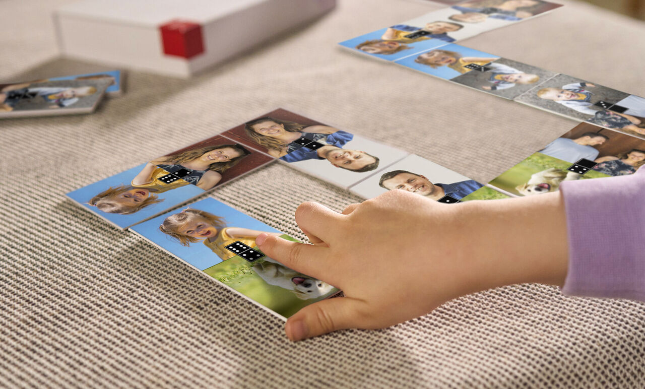 Ein Kind spielt mit personalisierten Dominosteinen auf einem Tisch, die Fotos von Freunden und Familie zeigen