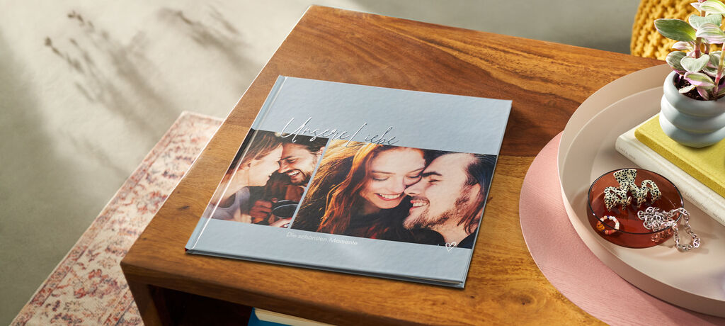 Ein offenes, liebevoll gestaltetes CEWE FOTOBUCH liegt auf einem Holztisch. Die Seiten zeigen fröhliche Momente und Erinnerungen.