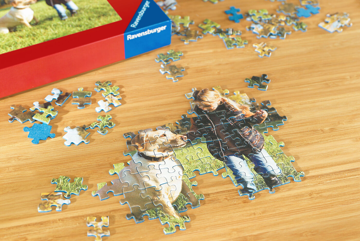Ein Kind spielt mit einem Hund, während Puzzlestücke auf einem Tisch verteilt sind.