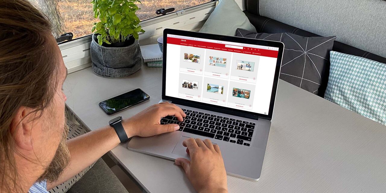 Mann sitzt an einem Tisch und arbeitet an einem Laptop, während sein Smartphone daneben liegt