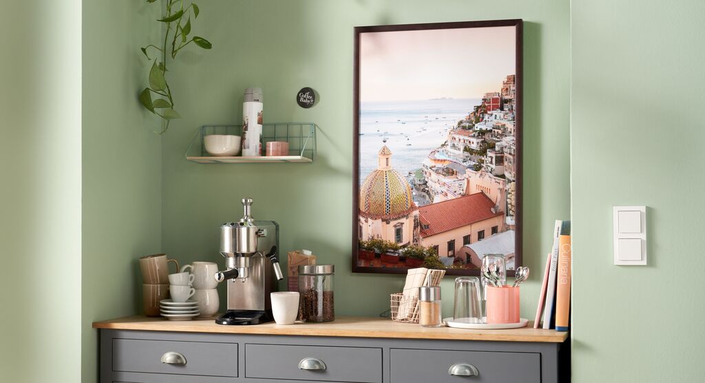 Eine schöne Küchenecke mit grünen Wänden, einer Kaffeemaschine und einem Wandbild aus Positano.