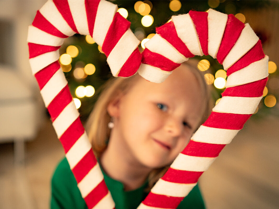 Ein Mädchen mit Zuckerstangen-Herz vor Weihnachtsbaum